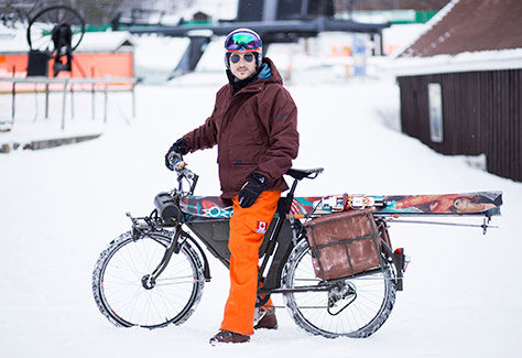 Winter biker at ski hill with downhill skis rigged on bike.